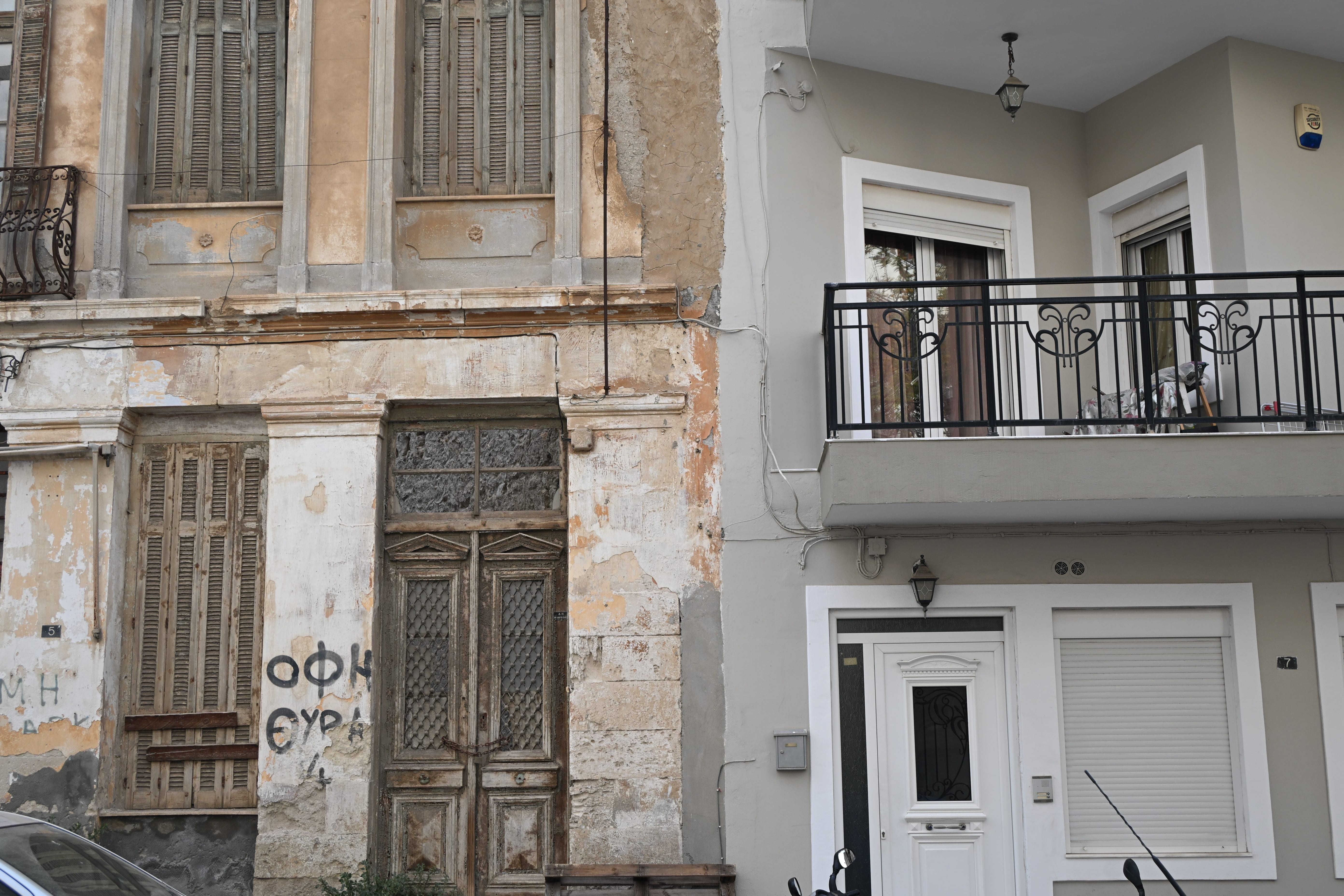 Faded apartment building with peeling paint stands next to a renovated whitewashed rental facade