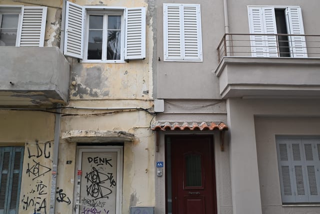 Graffiti tags on a weathered shutter beneath an immaculate whitewashed upper floor